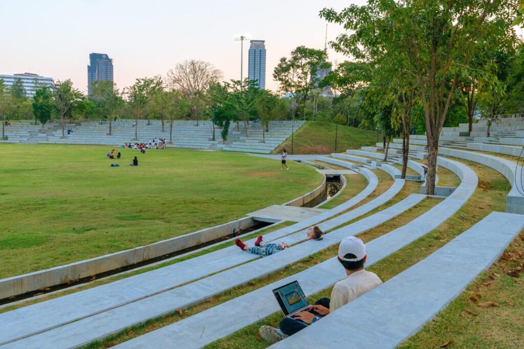 People relaxing at amphitheatre lawn in Benjakitti Park with Bangkok skyline in background